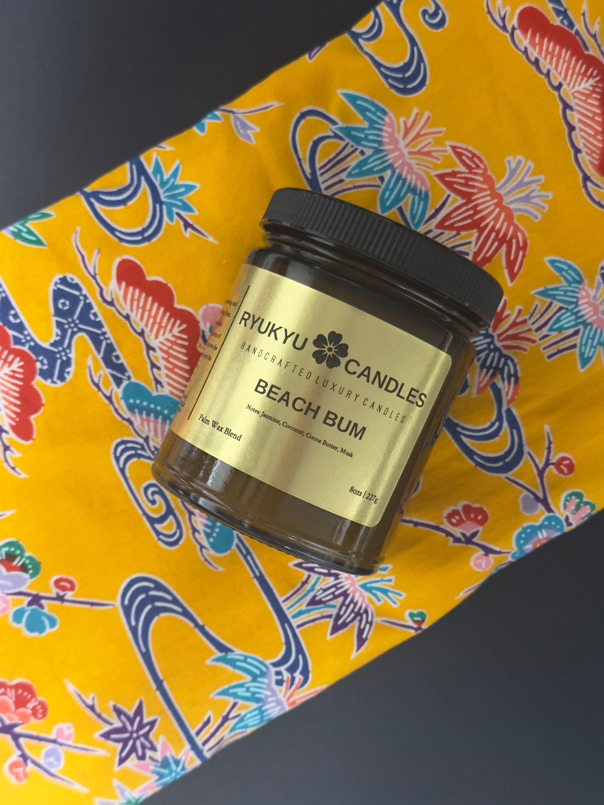 Jar of 'Beach Bum' candle from Rykyu Candles on a colorful Okinawan obi fabric background