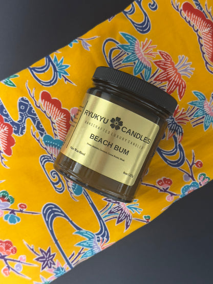 Jar of 'Beach Bum' candle from Rykyu Candles on a colorful Okinawan obi fabric background